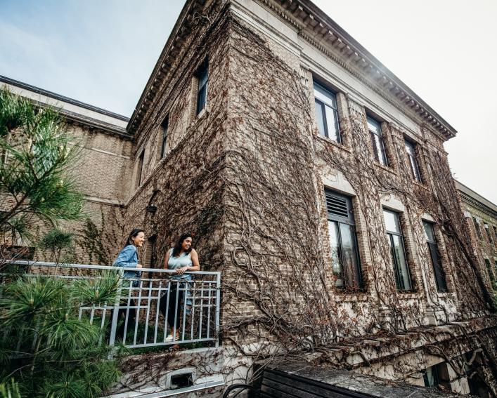 两名学生在阳台上，背景是爬满常春藤的植物科学大楼